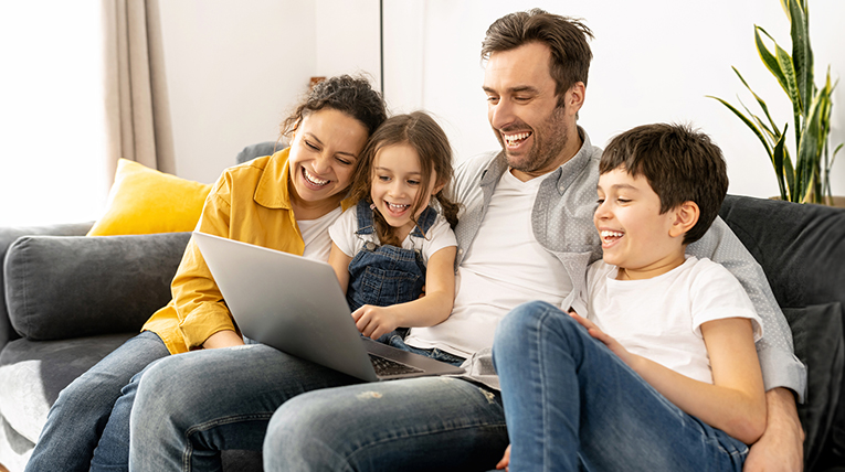 Happy family uses a laptop together on couch.